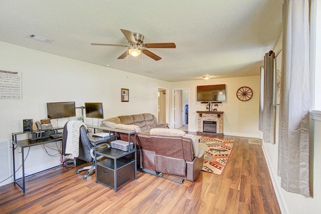 living area featuring visible vents, a glass covered fireplace, wood finished floors, ceiling fan, and a textured ceiling
