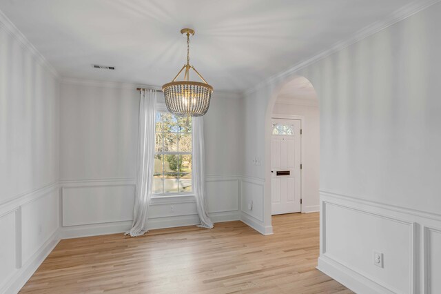 unfurnished dining area with arched walkways, light wood finished floors, ornamental molding, and visible vents