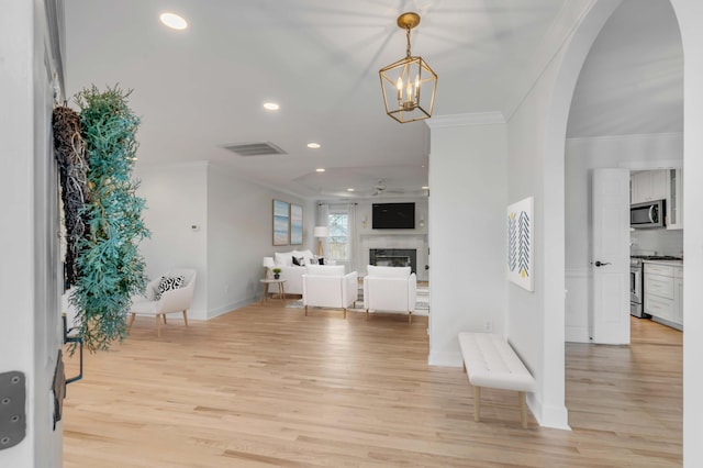 entryway with arched walkways, crown molding, light wood-type flooring, a fireplace, and recessed lighting