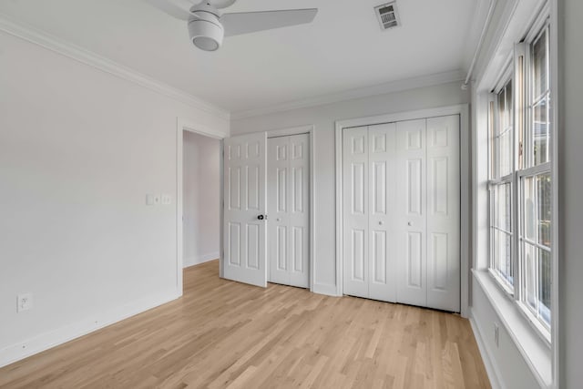 unfurnished bedroom with crown molding, multiple closets, visible vents, light wood-style flooring, and baseboards