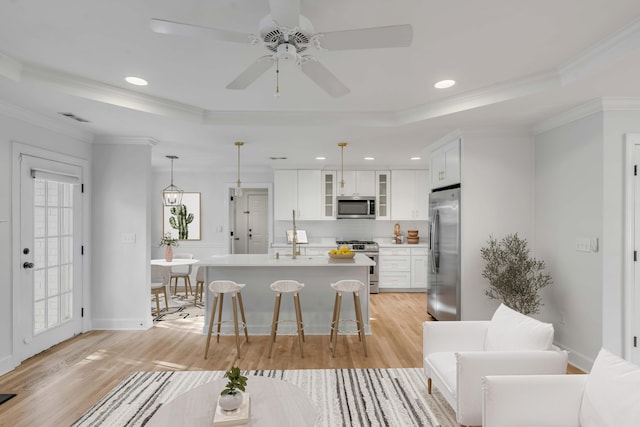 kitchen with stainless steel appliances, a raised ceiling, glass insert cabinets, and decorative light fixtures