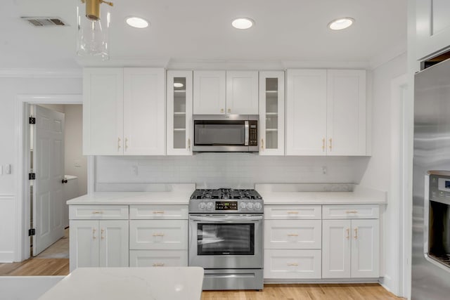 kitchen featuring visible vents, appliances with stainless steel finishes, glass insert cabinets, ornamental molding, and white cabinetry