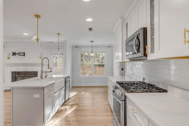 kitchen featuring a sink, white cabinets, hanging light fixtures, appliances with stainless steel finishes, and crown molding