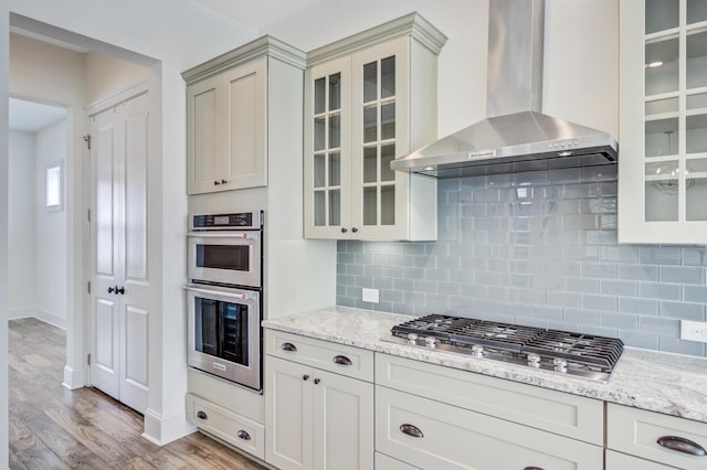 1485 Bourne Xing, Mount Pleasant, SC 29466 - kitchen featuring wall chimney range hood, appliances with stainless steel finishes, wood finished floors, decorative backsplash, and light stone countertops