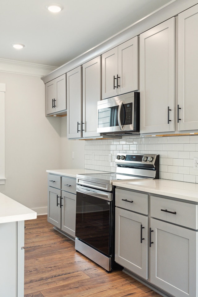 kitchen featuring gray cabinetry, dark hardwood / wood-style flooring, backsplash, appliances with stainless steel finishes, and ornamental molding