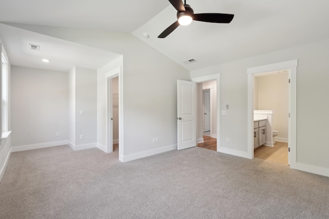 unfurnished bedroom with ceiling fan, light colored carpet, connected bathroom, and vaulted ceiling