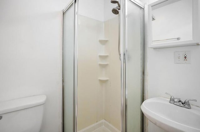 bathroom featuring toilet, a shower with shower door, and sink