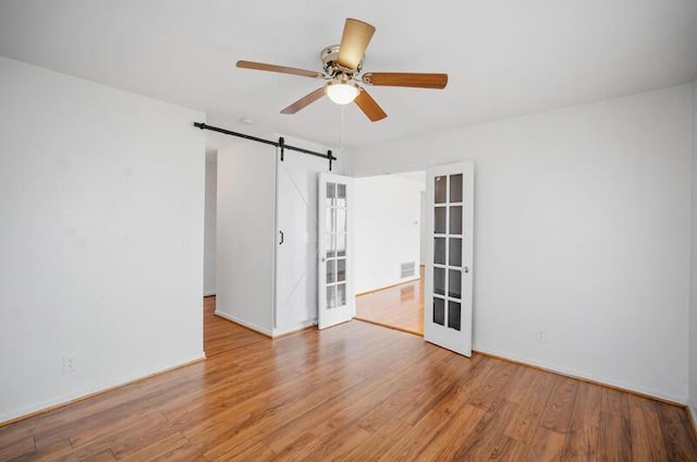 empty room with ceiling fan, a barn door, and light wood-type flooring