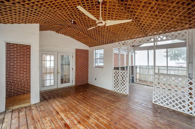 unfurnished room featuring lofted ceiling, ceiling fan, wood-type flooring, brick wall, and french doors