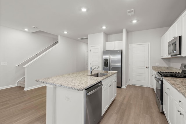 kitchen with white cabinets, appliances with stainless steel finishes, light wood-type flooring, and a kitchen island with sink