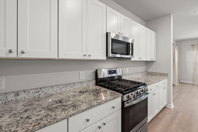 kitchen featuring light stone countertops, white cabinetry, stainless steel appliances, and light wood-type flooring