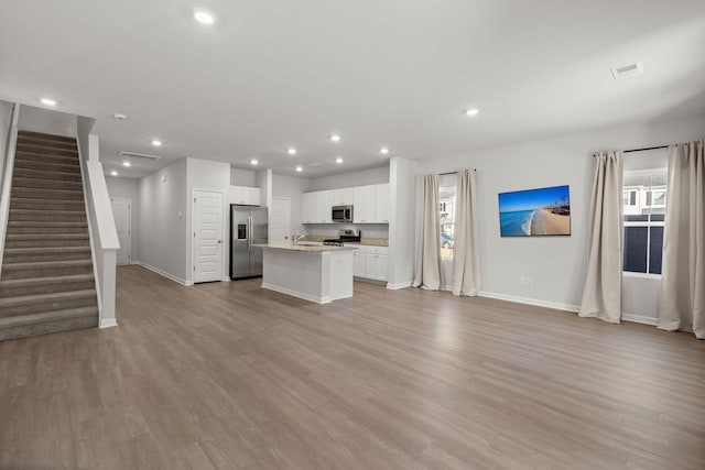 kitchen with white cabinets, light hardwood / wood-style floors, stainless steel appliances, and an island with sink