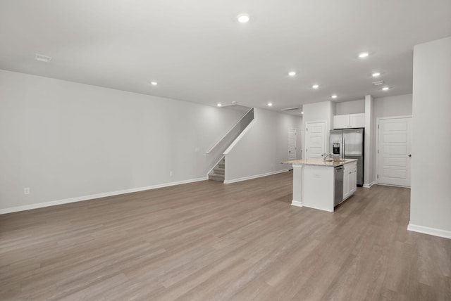 kitchen with light stone countertops, appliances with stainless steel finishes, a center island with sink, white cabinets, and light wood-type flooring