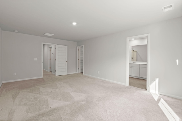 unfurnished bedroom featuring ensuite bathroom, a closet, and light colored carpet