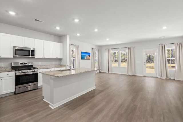 kitchen with a center island with sink, white cabinets, light stone countertops, appliances with stainless steel finishes, and wood-type flooring