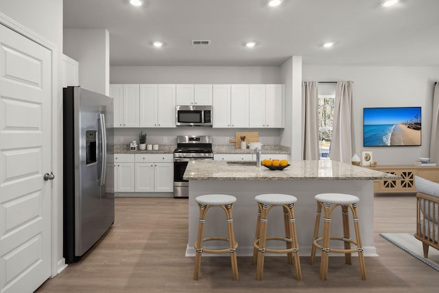 kitchen featuring appliances with stainless steel finishes, a center island with sink, white cabinetry, and light stone counters