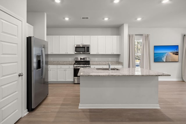 kitchen with white cabinetry, an island with sink, light stone countertops, and appliances with stainless steel finishes