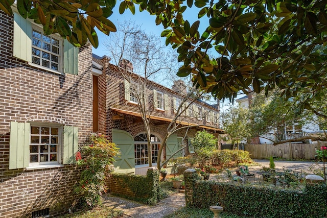 rear view of house featuring brick siding, a chimney, and fence