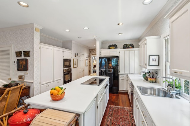 kitchen featuring a center island, ornamental molding, a sink, black appliances, and wallpapered walls