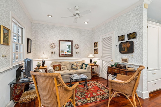 living area with dark wood finished floors, ornamental molding, a ceiling fan, wainscoting, and wallpapered walls