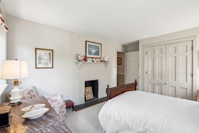 bedroom with concrete flooring, a fireplace with raised hearth, and a closet