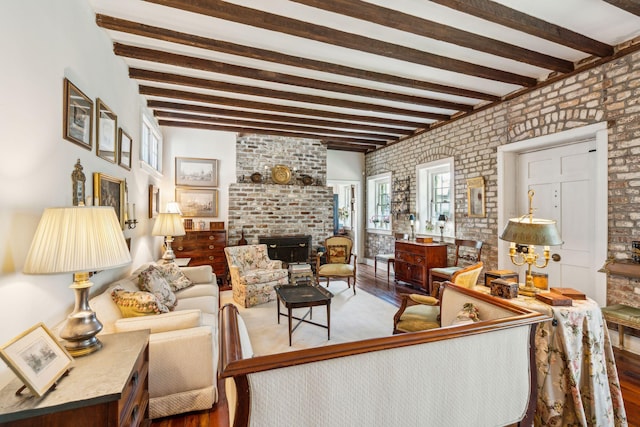 living area with a brick fireplace, brick wall, beam ceiling, and wood finished floors