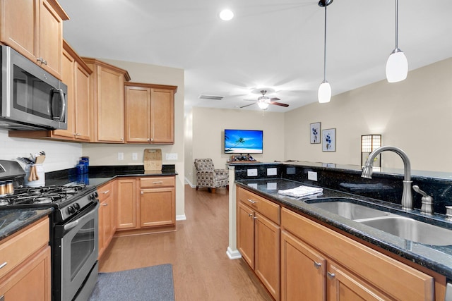 kitchen with sink, dark stone countertops, pendant lighting, stainless steel appliances, and light hardwood / wood-style floors