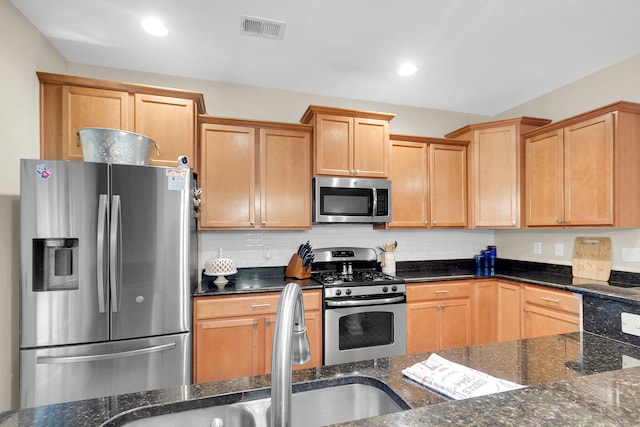 kitchen with appliances with stainless steel finishes, sink, dark stone countertops, and backsplash