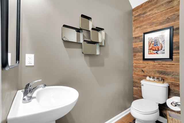 bathroom featuring toilet, wooden walls, and sink