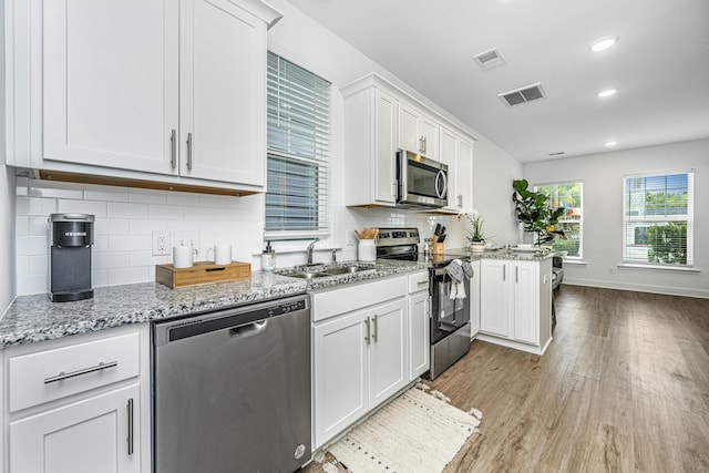 kitchen with light stone countertops, appliances with stainless steel finishes, backsplash, sink, and white cabinetry