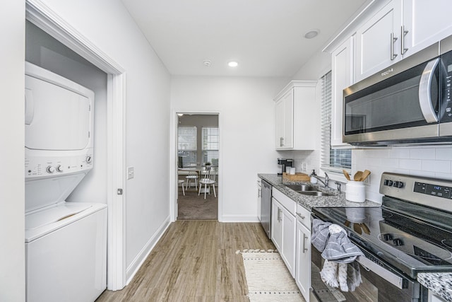 kitchen featuring sink, stacked washer and dryer, light stone counters, white cabinetry, and stainless steel appliances