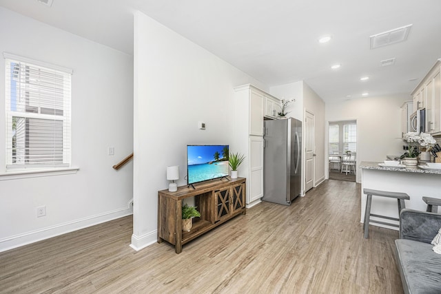 kitchen with a kitchen bar, light stone countertops, light wood-type flooring, stainless steel appliances, and white cabinets