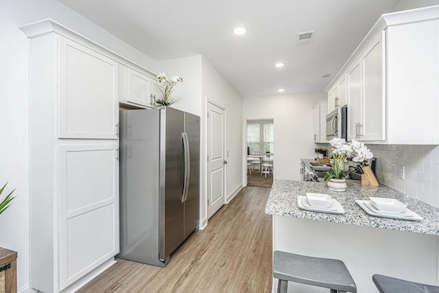 kitchen with appliances with stainless steel finishes, light wood-type flooring, white cabinetry, and light stone counters