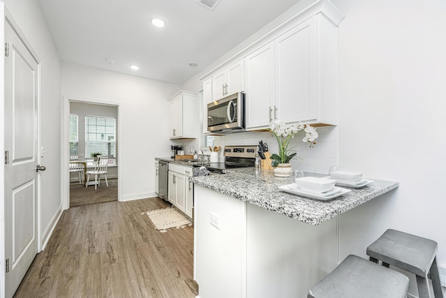 kitchen with a kitchen breakfast bar, stainless steel appliances, white cabinetry, and light hardwood / wood-style floors