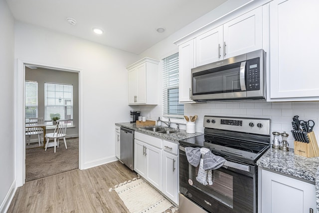 kitchen with light stone countertops, stainless steel appliances, white cabinetry, and sink