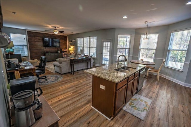 kitchen featuring dark hardwood / wood-style floors, an island with sink, sink, hanging light fixtures, and light stone counters