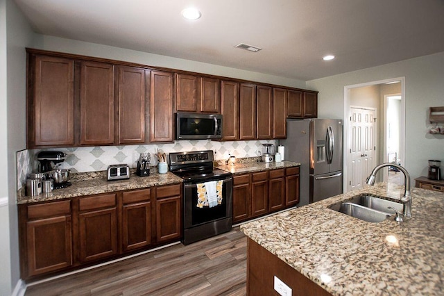 kitchen with sink, light stone counters, dark hardwood / wood-style floors, stainless steel appliances, and decorative backsplash