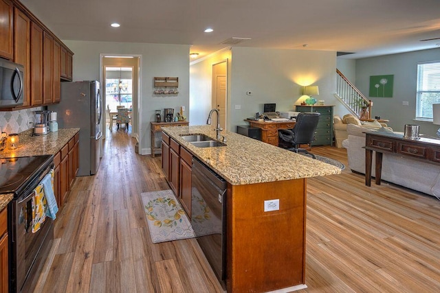 kitchen featuring sink, a center island with sink, stainless steel appliances, light stone countertops, and light hardwood / wood-style floors