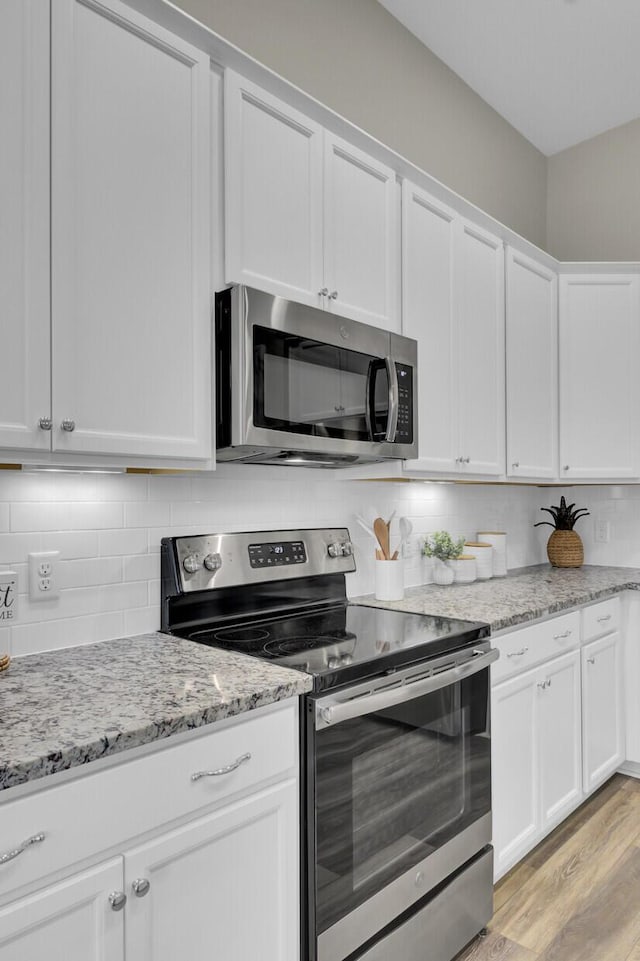 kitchen featuring tasteful backsplash, light stone counters, stainless steel appliances, light hardwood / wood-style flooring, and white cabinets