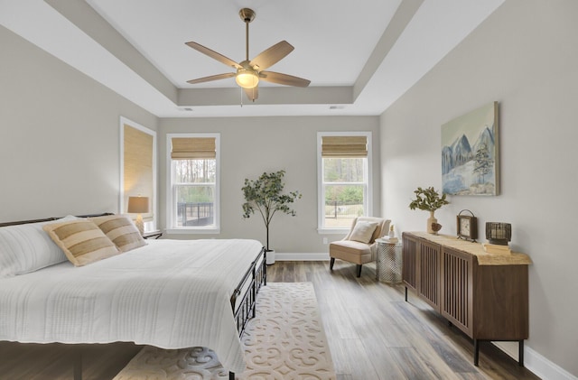 bedroom with hardwood / wood-style flooring, ceiling fan, multiple windows, and a tray ceiling