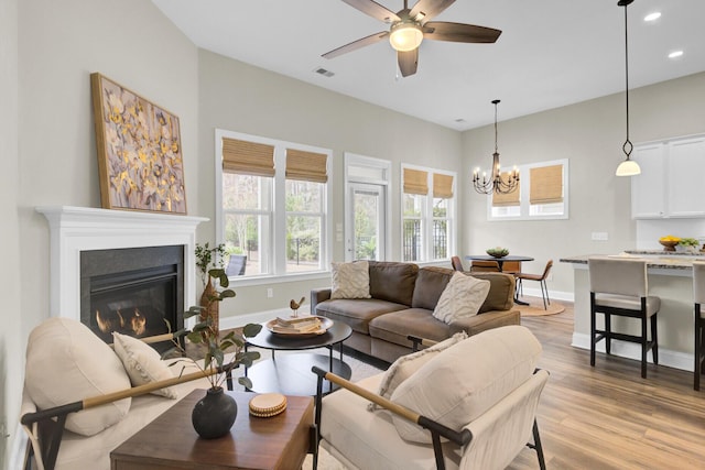 living room with ceiling fan with notable chandelier and light hardwood / wood-style flooring