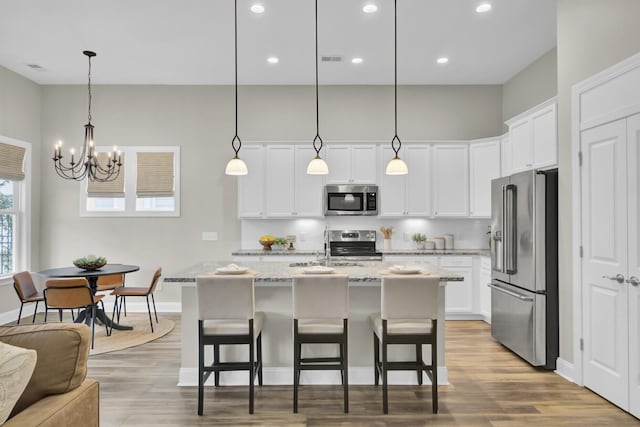 kitchen featuring white cabinetry, stainless steel appliances, a notable chandelier, decorative light fixtures, and a kitchen island with sink