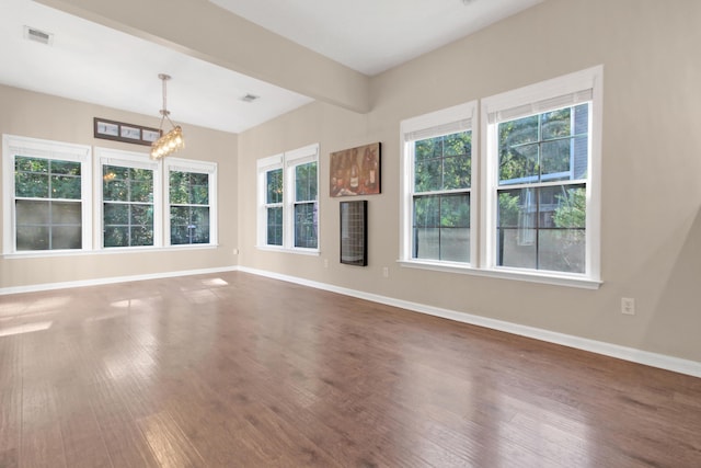 spare room with wood-type flooring, plenty of natural light, and a notable chandelier