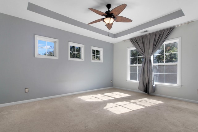 empty room with ceiling fan, light colored carpet, and a tray ceiling