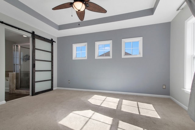 unfurnished room with carpet, a barn door, a raised ceiling, and ceiling fan