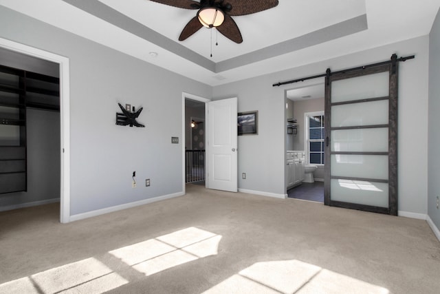 unfurnished bedroom featuring ensuite bath, ceiling fan, a barn door, a spacious closet, and a closet