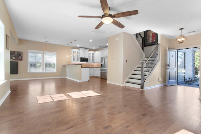 unfurnished living room featuring wood-type flooring, ceiling fan with notable chandelier, and a healthy amount of sunlight