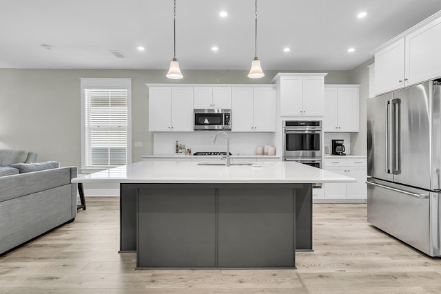 kitchen with hanging light fixtures, white cabinetry, a center island with sink, and stainless steel appliances