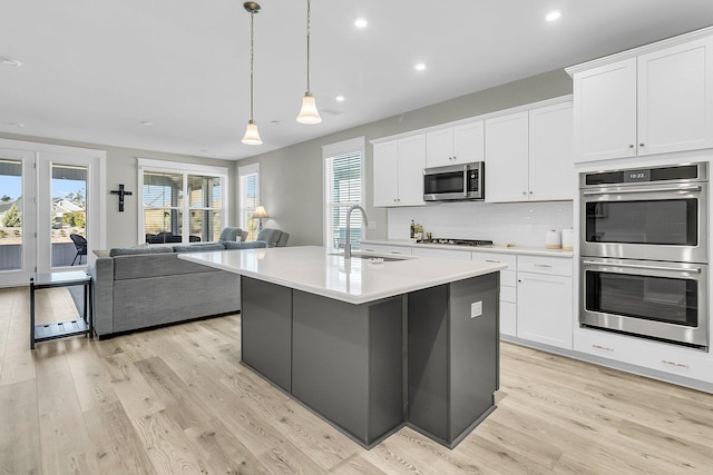 kitchen with appliances with stainless steel finishes, sink, white cabinetry, hanging light fixtures, and an island with sink