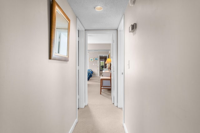 hall with light colored carpet, baseboards, and a textured ceiling